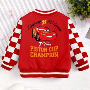 May include: Red and white checkered bomber jacket with a red Lightning McQueen graphic on the back. The graphic includes the text "Lightning 95 McQueen", "7 Time Piston Cup Champion", and a cartoon image of the race car.