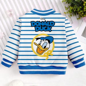May include: A white and blue striped sweatshirt with a blue collar and cuffs. The sweatshirt features a cartoon image of Donald Duck with the text "Disney DONALD DUCK" above the image.