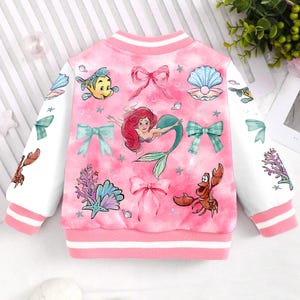 May include: Pink and white bomber jacket with a colorful print of Ariel the mermaid, Sebastian the crab, Flounder the fish, and other sea-themed imagery. The jacket has a white collar and cuffs with pink stripes.