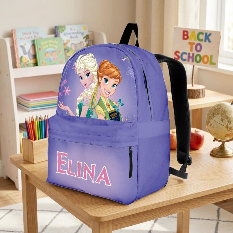 Op de afbeelding: Een paarse rugzak met een afbeelding van twee geanimeerde personages met blond en kastanjebruin haar. Het voorvak toont de naam ELINA in grote roze letters. De tas heeft zwarte schouderbanden en een voorvak met ritssluiting.