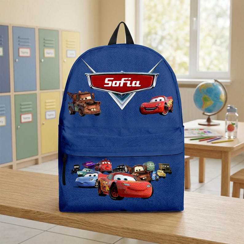 May include: A blue backpack with a black handle, featuring characters from the film Cars. The backpack has a front pocket with various Cars characters. The name "Sofia" is displayed in a red and white emblem.
