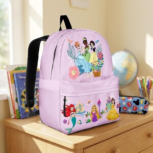 May include: A light purple backpack featuring a colorful illustration of Disney princesses. The backpack has a black handle and straps, a front pocket, and a main compartment. The design includes Ariel, Rapunzel, and Belle.