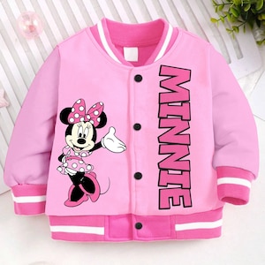 May include: Pink children's jacket with a white stripe on the collar and cuffs. The jacket has a button closure and features a Minnie Mouse graphic and the word "MINNIE" printed on the front.