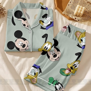 May include: Light green pajama set featuring Mickey Mouse, Donald Duck, and Goofy. The button-down top and matching pants have a white trim and are covered in cartoon character faces. The set is made of a soft material.