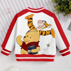 May include: A white and red baseball jacket with a Winnie the Pooh and Tigger design on the back. The design features Winnie the Pooh holding a jar of honey and Tigger standing on his back.