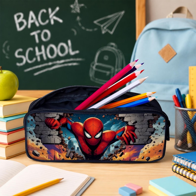 May include: A rectangular pencil case featuring a graphic of Spider-Man breaking through a brick wall. The case is filled with several colored pencils in shades of red, white, yellow, and blue, standing upright against a dark interior lining.