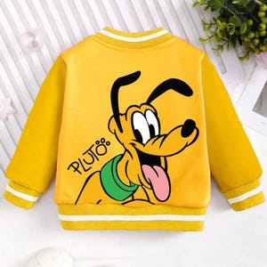 May include: Yellow children's jacket with a cartoon image of Pluto the dog on the back. The jacket has a white stripe around the collar and cuffs. The text "PLUTO" is printed on the jacket.