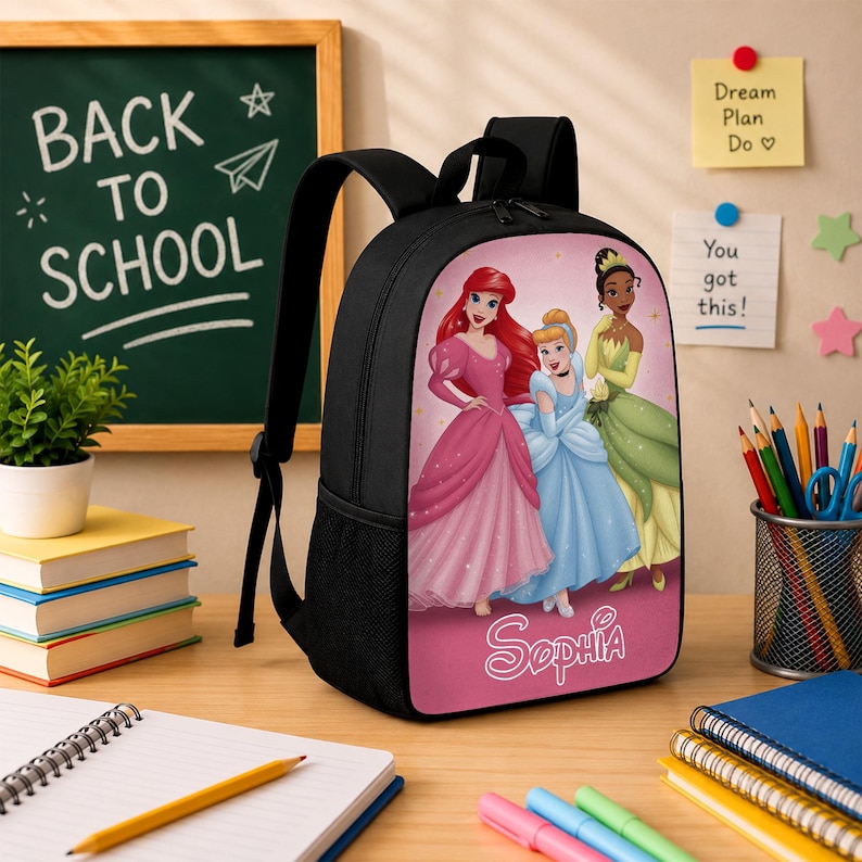 May include: A black backpack featuring a graphic print of three animated princesses in pink, blue, and green gowns on the front panel. The name Sophia is printed in white script at the bottom of the graphic. The bag has black straps and side mesh pockets.