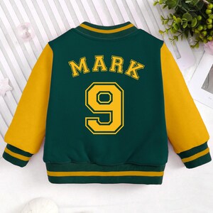 May include: A green and yellow baseball jacket with the name "Mark" and the number "9" on the back.
