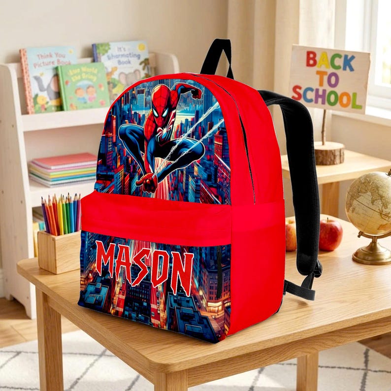 K&ouml;nnte beinhalten: Ein leuchtend roter Rucksack mit einer Grafik des Superhelden Spider-Man in einer dynamischen Pose vor einer Skyline. Die Vordertasche zeigt den Namen MASON in fetten, gezackten wei&szlig;en Buchstaben vor einem detaillierten Stadtbild.