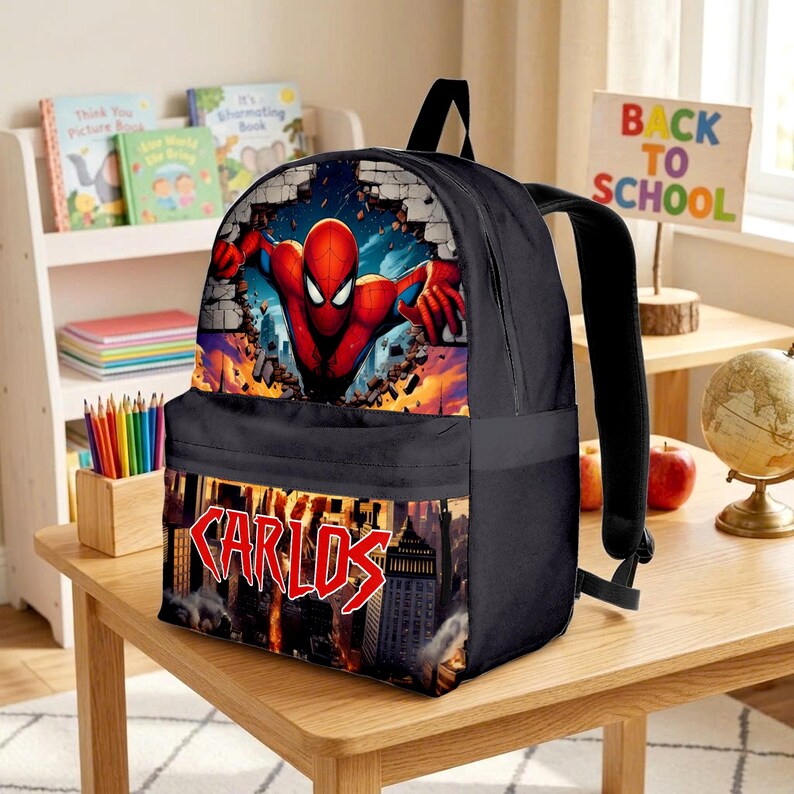 May include: A black backpack featuring a graphic of a red and blue superhero bursting through a brick wall. The lower pocket displays a city skyline at sunset with the name CARLOS printed in a bold, red, jagged font across the center of the bag.