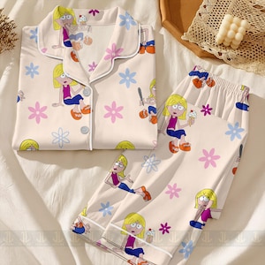 Pu&ograve; includere: Un completo pigiama a due pezzi con stampa di personaggi dei cartoni animati. Il set comprende una camicia con bottoni e pantaloni, entrambi color crema con un motivo ripetuto del personaggio, fiori e stelle. I pigiami hanno finiture bianche.