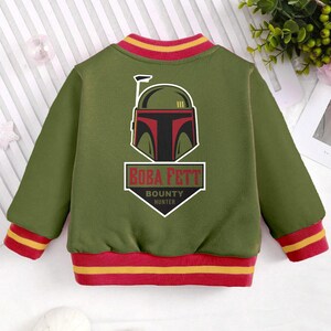 May include: Green bomber jacket with red and yellow stripes on the cuffs and collar. The back of the jacket features a graphic of Boba Fett's helmet with the text "BOBA FETT BOUNTY HUNTER".