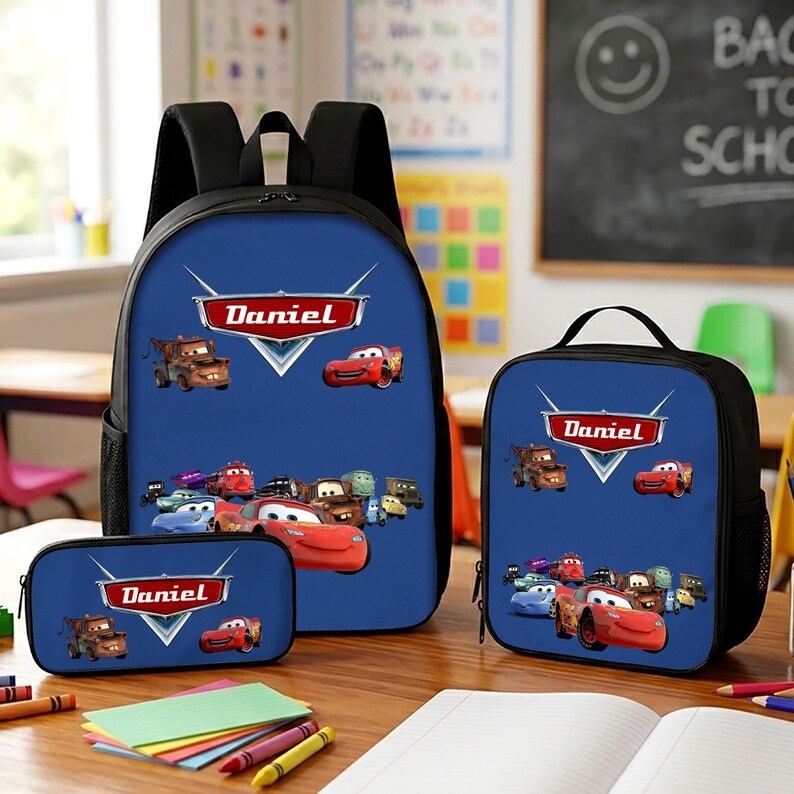 K&ouml;nnte beinhalten: Ein Set aus blauem Rucksack, Lunchtasche und Federm&auml;ppchen mit den Charakteren aus dem Film Cars und dem Namen Daniel in einem roten Logo. Jeder Artikel zeigt eine Gruppe bunter animierter Fahrzeuge auf einem einfarbig blauen Hintergrund.