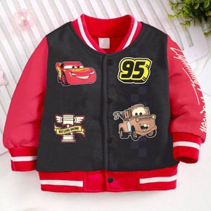 May include: Black and red bomber jacket with a Cars theme. The jacket features Lightning McQueen, Mater, and the number 95. The jacket has a white stripe on the collar and cuffs.