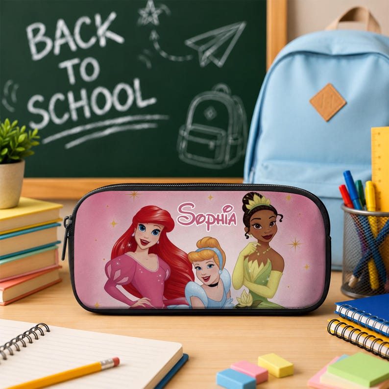 May include: A rectangular pencil case with a pink background featuring illustrations of Ariel, Cinderella, and Tiana. The name Sophia is printed in white script above the characters. The case has a black zip and black trim along the edges.
