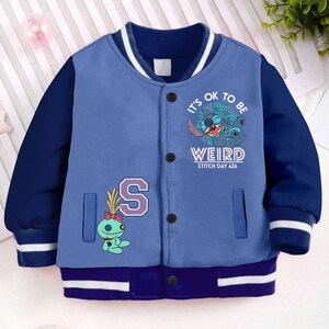 May include: Blue and white baseball jacket with a blue Stitch character graphic and the text "It's OK to be WEIRD Stitch Day 626".