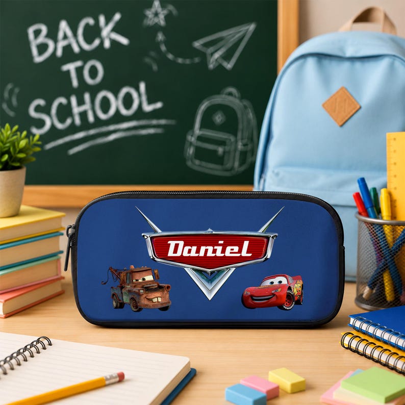 May include: A blue rectangular pencil case featuring the Disney Pixar Cars logo with the name Daniel printed in white text. The design includes illustrations of the characters Mater and Lightning McQueen on a solid blue background with a black zipper.