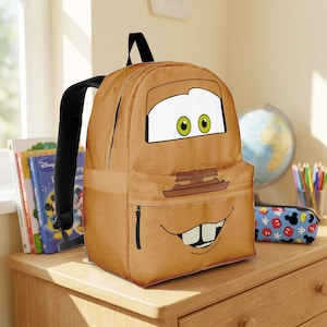 Puede incluir: Una mochila marr&oacute;n con un dise&ntilde;o de cara de coche de dibujos animados, con detalles blancos, verdes y negros. La mochila tiene correas negras y un bolsillo con cremallera. El dise&ntilde;o est&aacute; inspirado en el personaje Mate de la pel&iacute;cula Cars.