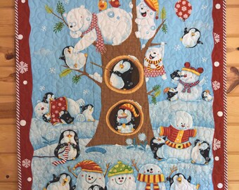 May include: A rectangular quilt featuring a winter scene with polar bears, penguins, and snowmen. The central brown tree has two hollows containing penguins. The border is dark red with white snowflakes and a striped edge, quilted with wavy lines.