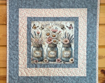 May include: A square fabric wall hanging featuring a central panel with three mason jars filled with flowers, labeled Faith, Hope, and Love. The text Today I Choose is printed above. The quilt has a light floral border and a blue stippled outer border.