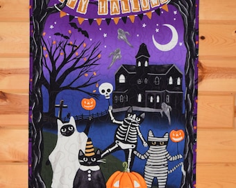 Può includere: Una trapunta di Halloween viola e nera con uno striscione che recita "Happy Halloween". La trapunta presenta una casa stregata, una luna crescente e quattro gatti vestiti in costume. Un gatto è un fantasma, uno è uno scheletro, uno è una mummia e uno indossa un cappello da strega.