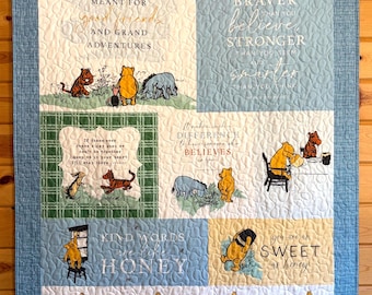 May include: A Winnie the Pooh themed quilt with various quotes and illustrations. The quilt features characters like Pooh, Piglet, and Eeyore, with text that reads "Life was meant for good friends and grand adventures."