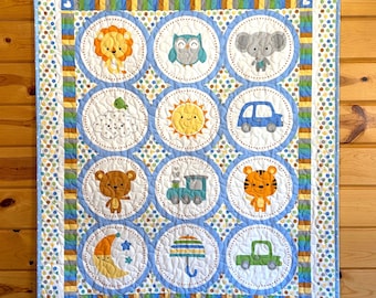 May include: A baby quilt with a repeating pattern of circular designs featuring various animals, vehicles, and celestial bodies. The quilt has a blue and white color scheme with accents of yellow, orange, and green. The quilt is hanging on a wooden wall.