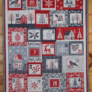 May include: A festive Christmas advent calendar quilt with a red, white, and gray color scheme. The quilt features 24 numbered squares with holiday-themed images like houses, trees, snowflakes, and birds. The quilt is bordered with a gray and red fabric.