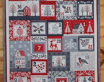 May include: A festive Christmas advent calendar quilt with a red, white, and gray color scheme. The quilt features 24 numbered squares with holiday-themed images like houses, trees, snowflakes, and birds. The quilt is bordered with a gray and red fabric.