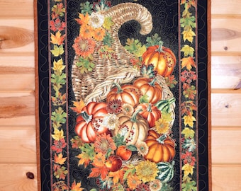 May include: A rectangular fabric wall hanging featuring a black background with a central cornucopia overflowing with orange pumpkins, autumn leaves, and flowers. The word Thankful is printed in gold script at the top, framed by a border of leaves.