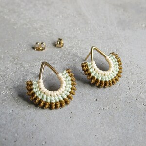 May include: A pair of gold earrings with a teardrop shape. The earrings are made of woven thread in shades of green, white, and gold.