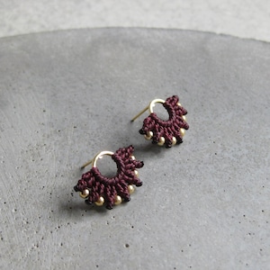 May include: A pair of small, burgundy-coloured earrings with gold beads. The earrings are made of a delicate, crocheted material.