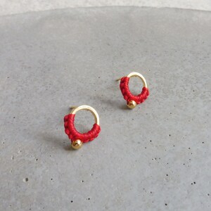 May include: A pair of red and gold earrings with a small circle design. The earrings are made of a thin gold wire with a small red bead in the centre.