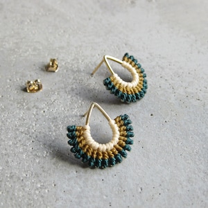 May include: A pair of teardrop-shaped earrings with a gold wire frame and a woven design of teal, white, and gold thread.