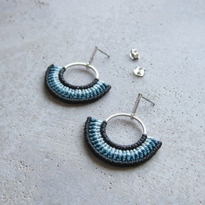May include: A pair of silver hoop earrings with a blue and black macrame design. The earrings are hanging from a silver post.