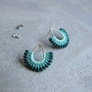 May include: A pair of teardrop-shaped earrings with a silver post and a green and blue ombre design. The earrings are made of a woven material and have a delicate, feminine look.