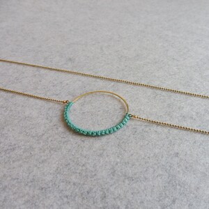 May include: A gold chain necklace with a teal crocheted circle pendant.