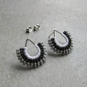 May include: A pair of silver earrings with a teardrop shape and a beaded design in shades of grey, black, and white.