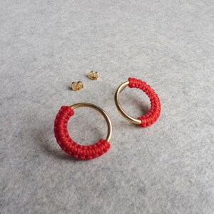 May include: A pair of red and gold hoop earrings. The hoops are made of a thin gold wire and are wrapped with red cord.
