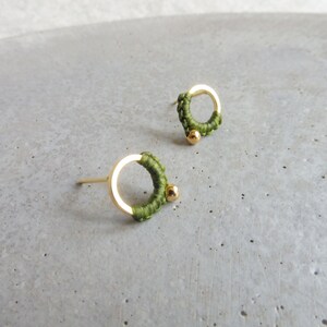 May include: A pair of gold-toned earrings with green thread wrapped around the circular metal part. Each earring has a small gold bead at the bottom.