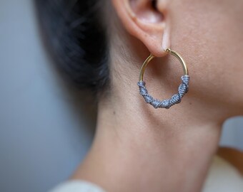 Aros gruesos dorados con detalle de fibra de macramé en gris. Joyería bohemia moderna y chic.