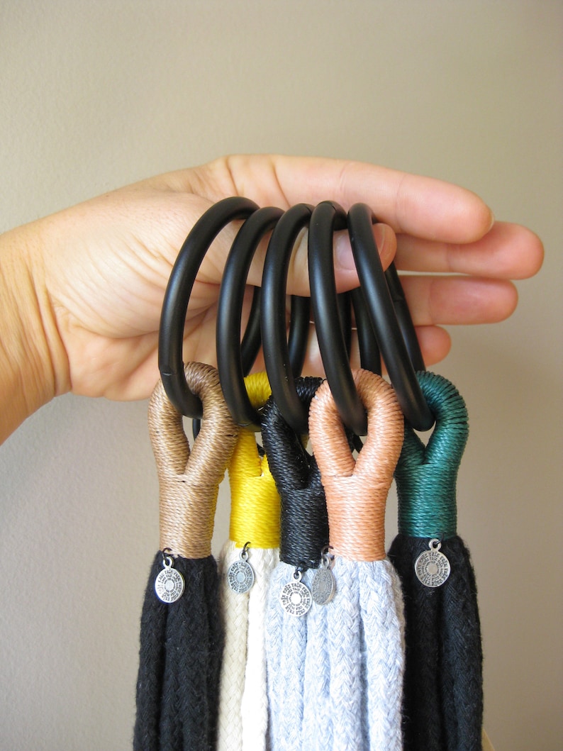 May include: A set of six macrame wall hangings with black, brown, yellow, green, and white rope. Each hanging has a silver charm with a circular design.
