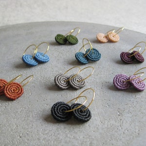 May include: Assortment of handmade earrings with different colored spiral designs. The earrings are made with a variety of colors, including blue, green, purple, and orange. Each earring is made with a gold hoop.