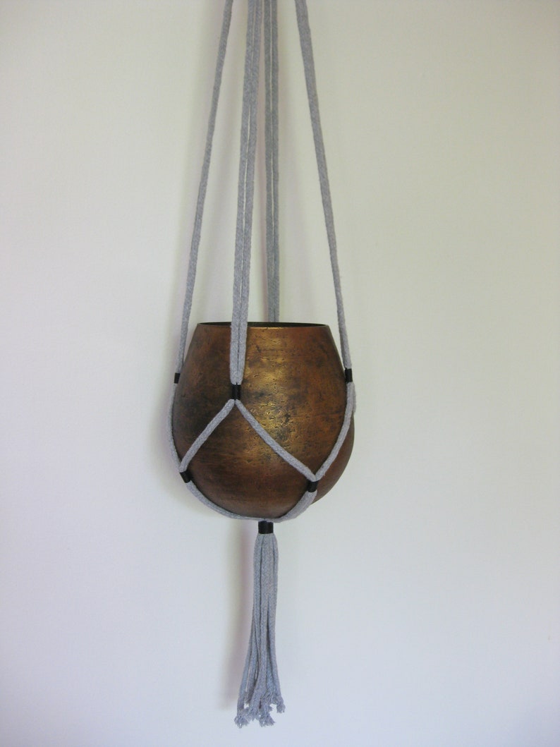 May include: A gray macrame plant hanger with a brown ceramic pot. The hanger has a tassel at the bottom.