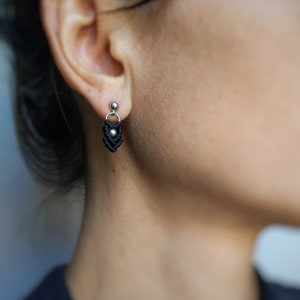 May include: A pair of black and silver earrings with a small, knotted design. The earrings are dangling from the earlobe.