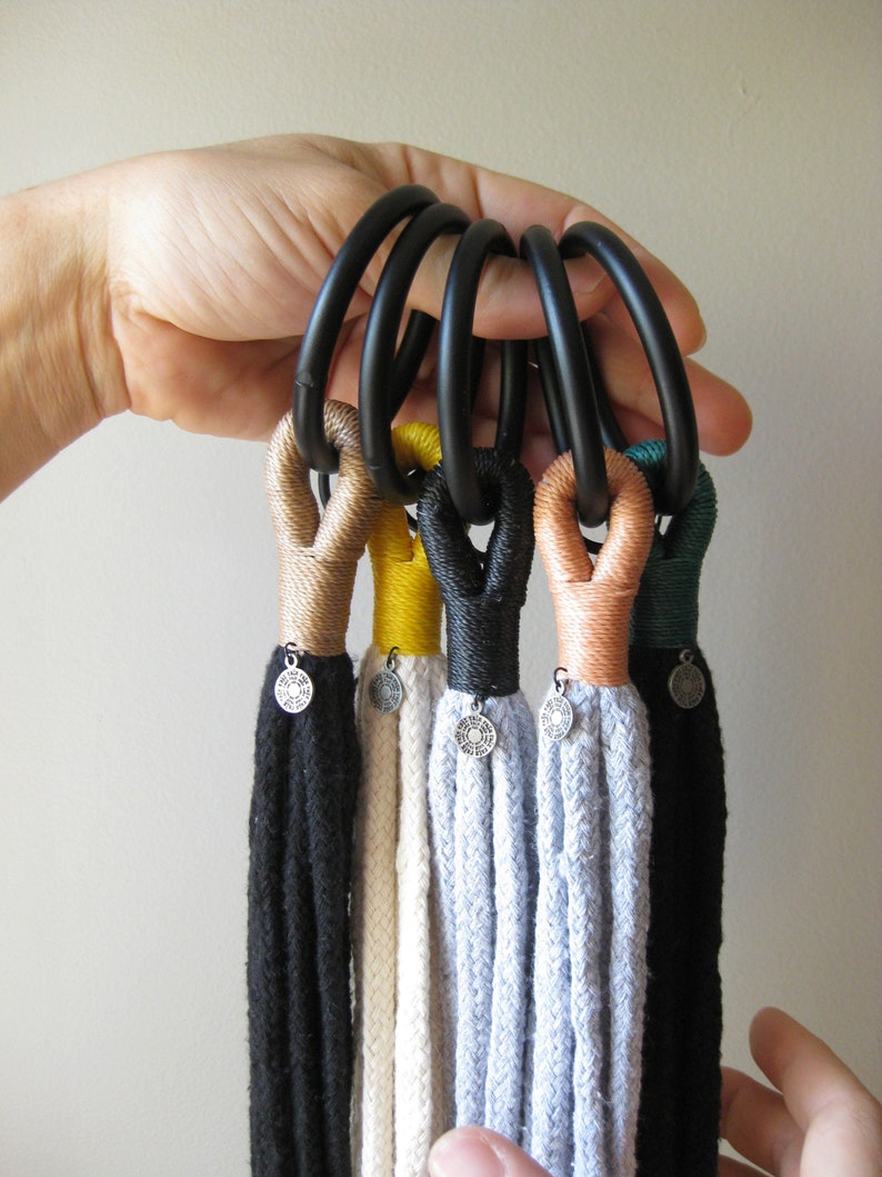 May include: Six black rope macrame plant hangers with different colored tassels. The tassels are black, white, light blue, beige, yellow, and green.