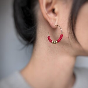 May include: Gold hoop earrings with red beaded accents. The earrings are worn in a person's ear.