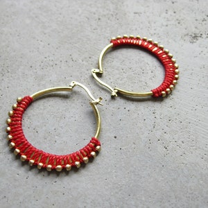 May include: A pair of gold hoop earrings with red string and gold beads around the hoop.