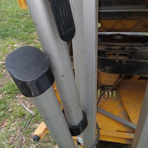 May include: Close-up of a silver and black metal folding ladder with a black rubber foot pad. The ladder is folded and resting on a yellow surface.